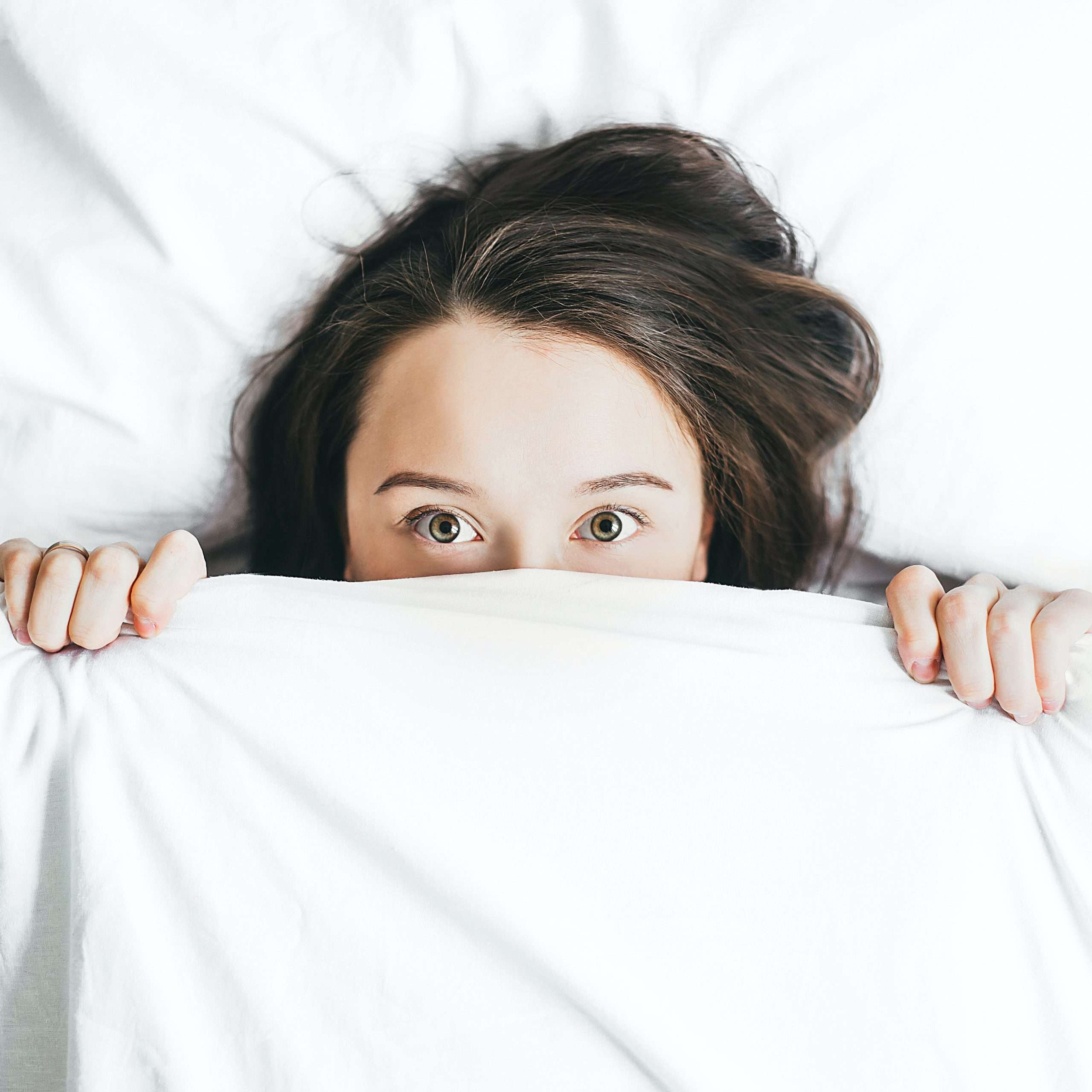 Woman in bed peeking over her sheets