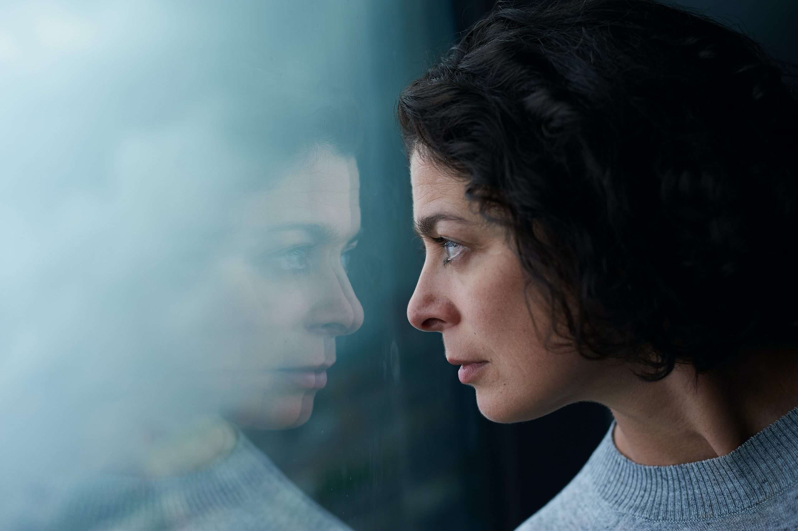 Woman with mental health issues looking at her reflection in a window