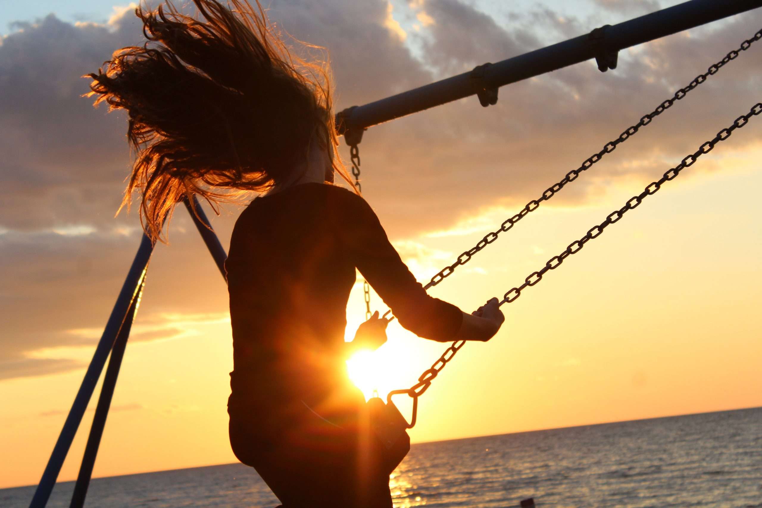 Woman on swing with sunset over the ocean in background