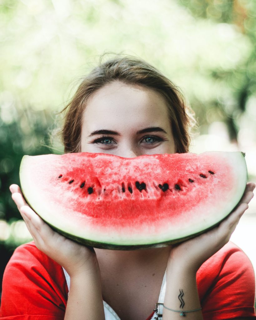 Woman with a watermelon infront of her face in the shape of a smile